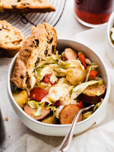 a bowl of Irish sausage, cabbage, and potatoes with Irish soda bread and Guinness