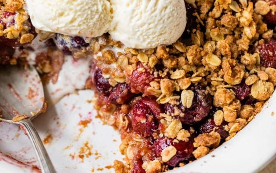 homemade sweet cherry crisp with a serving removed and topped with three scoops of vanilla ice cream