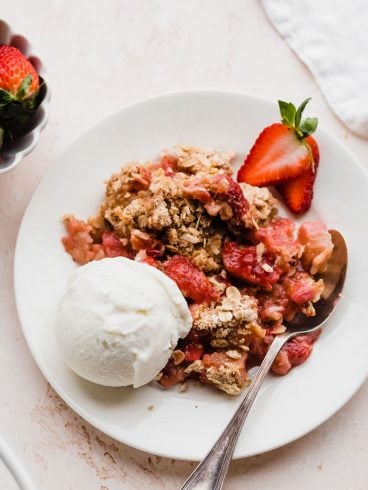 Grandma's Strawberry Rhubarb Crisp on a plate with ice cream and a spoon