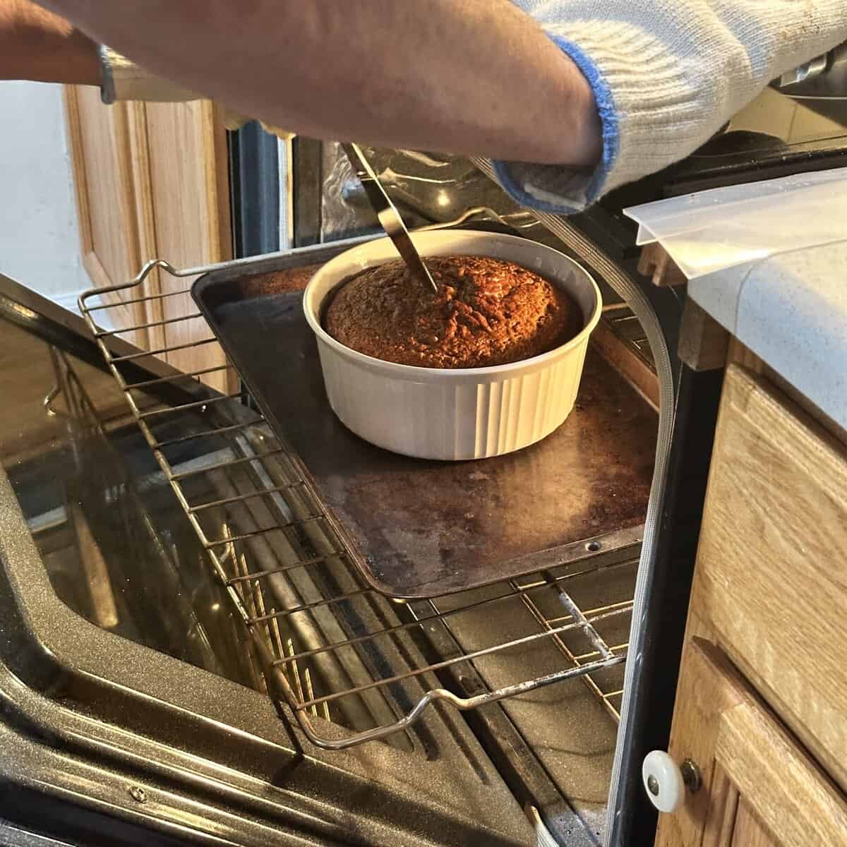 A person wearing an oven mitt checks a cake’s doneness with a knife in an oven.