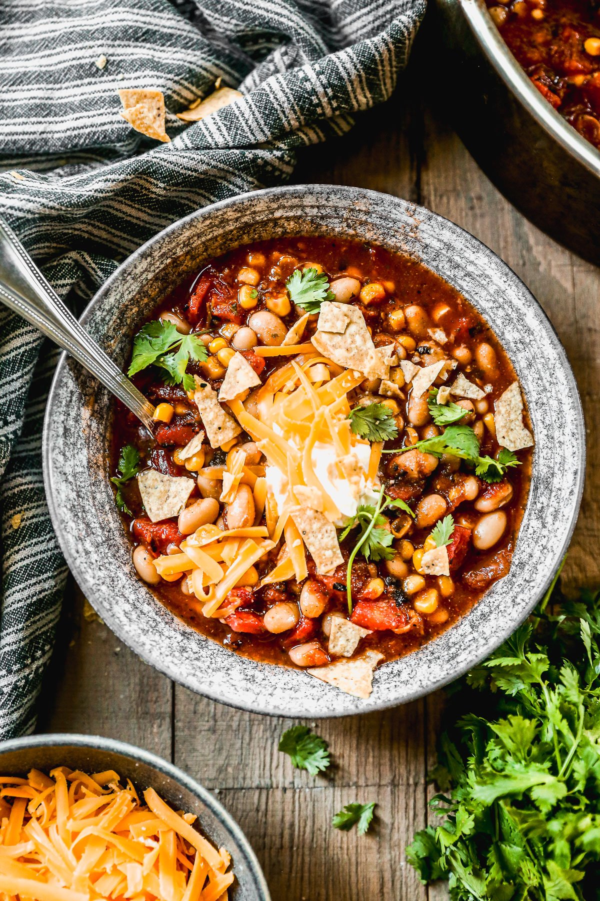 A bowl of taco soup topped with shredded cheese, tortilla chips, cilantro, and sour cream sits on a wooden table.