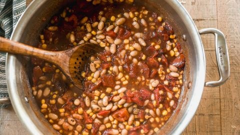 A pot of taco soup with beans, corn, tomatoes, and a wooden spoon stirring the mixture.