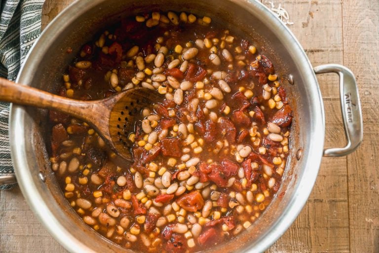 A pot of taco soup with beans, corn, tomatoes, and a wooden spoon stirring the mixture.