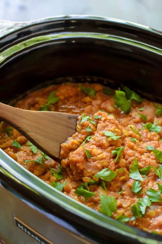 An easy and healthy slow cooker recipe for cauliflower curry with red lentils. Just toss the ingredients into your crock pot, and you are good to go! #slowcooker #crockpot #cauliflower #curry #healthy using a wooden spoon to stir healthy cauliflower curry in a slow cooker