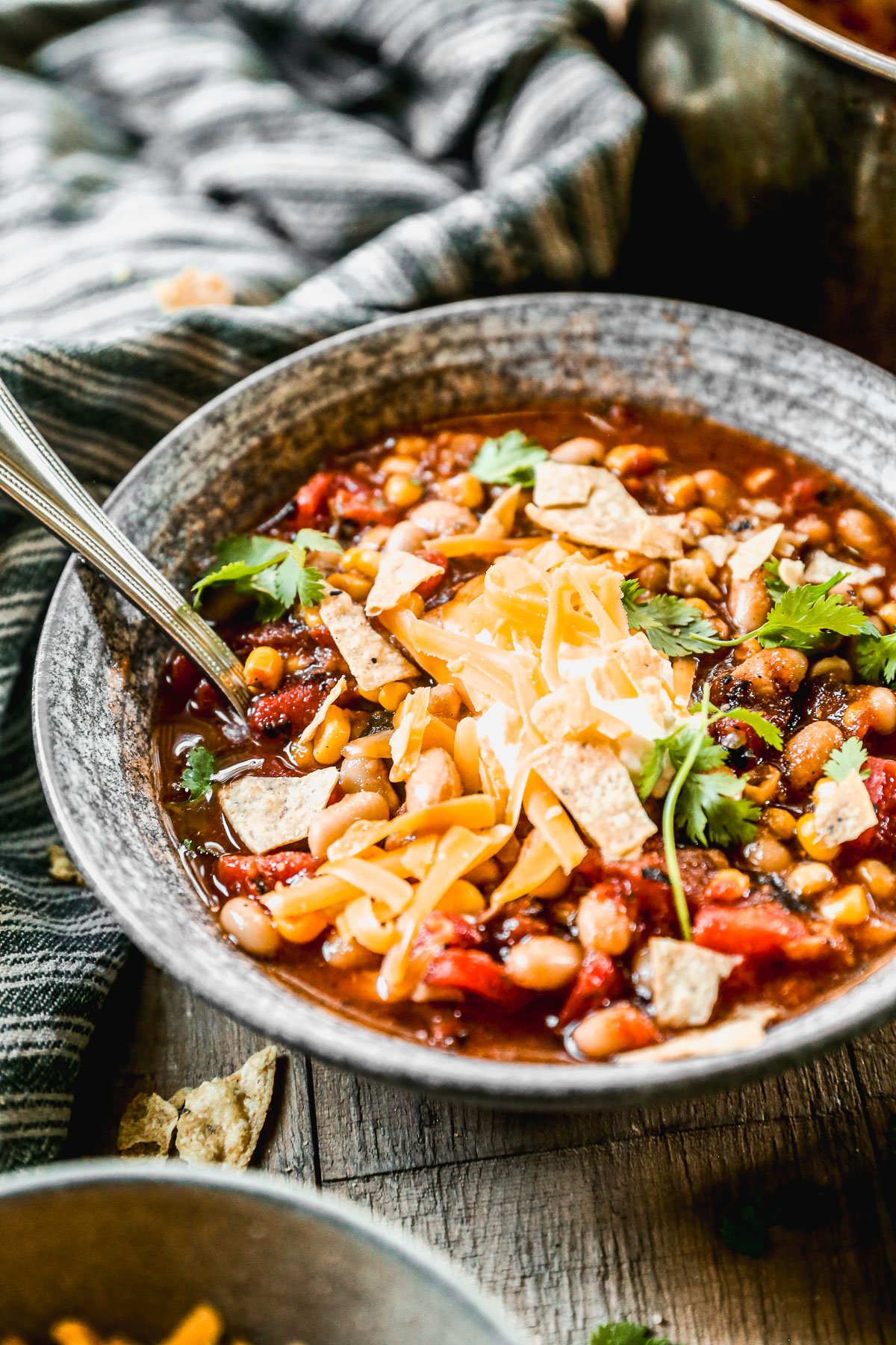 A bowl of taco soup topped with shredded cheese, tortilla chips, and cilantro, with a spoon inside.
