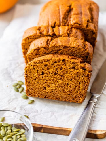 slices of low fat pumpkin bread on a piece of white parchment baking paper with a knife and pumpkin seeds