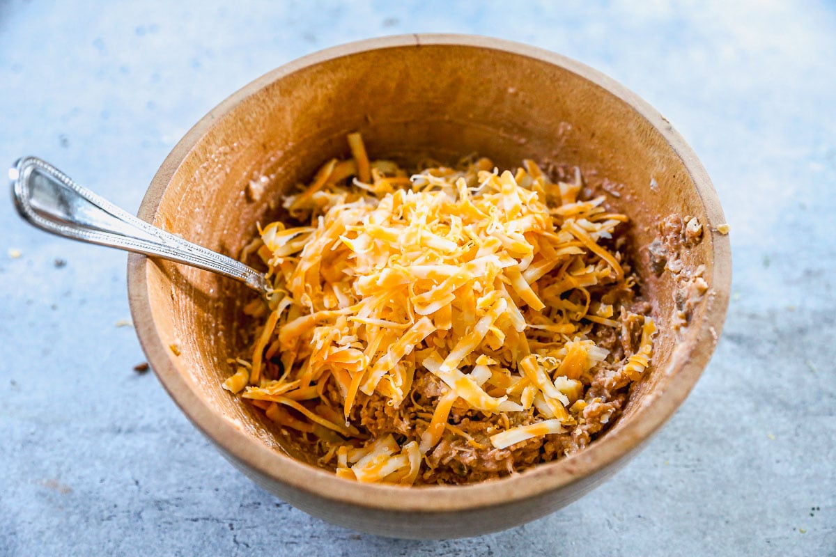 A wooden bowl filled with shredded cheese and a chicken, with a metal spoon inside.
