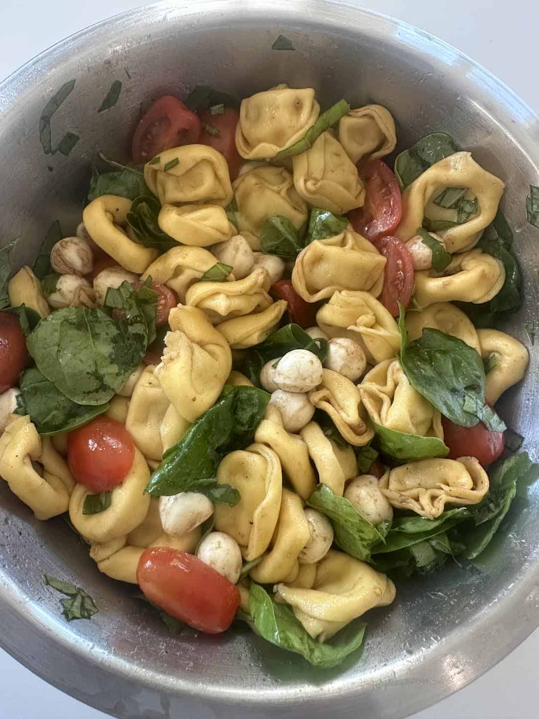 A bowl of tortellini pasta salad with spinach, cherry tomatoes, mozzarella balls, and basil.