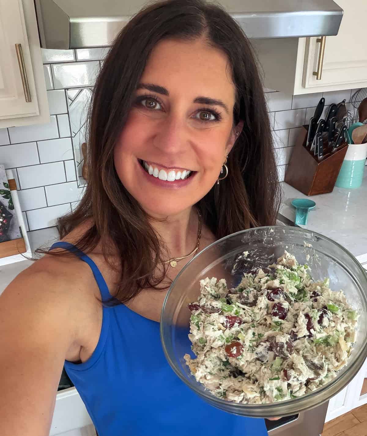 Erin Clarke in blue top smiling and holding a bowl of salad in a bright, modern kitchen.