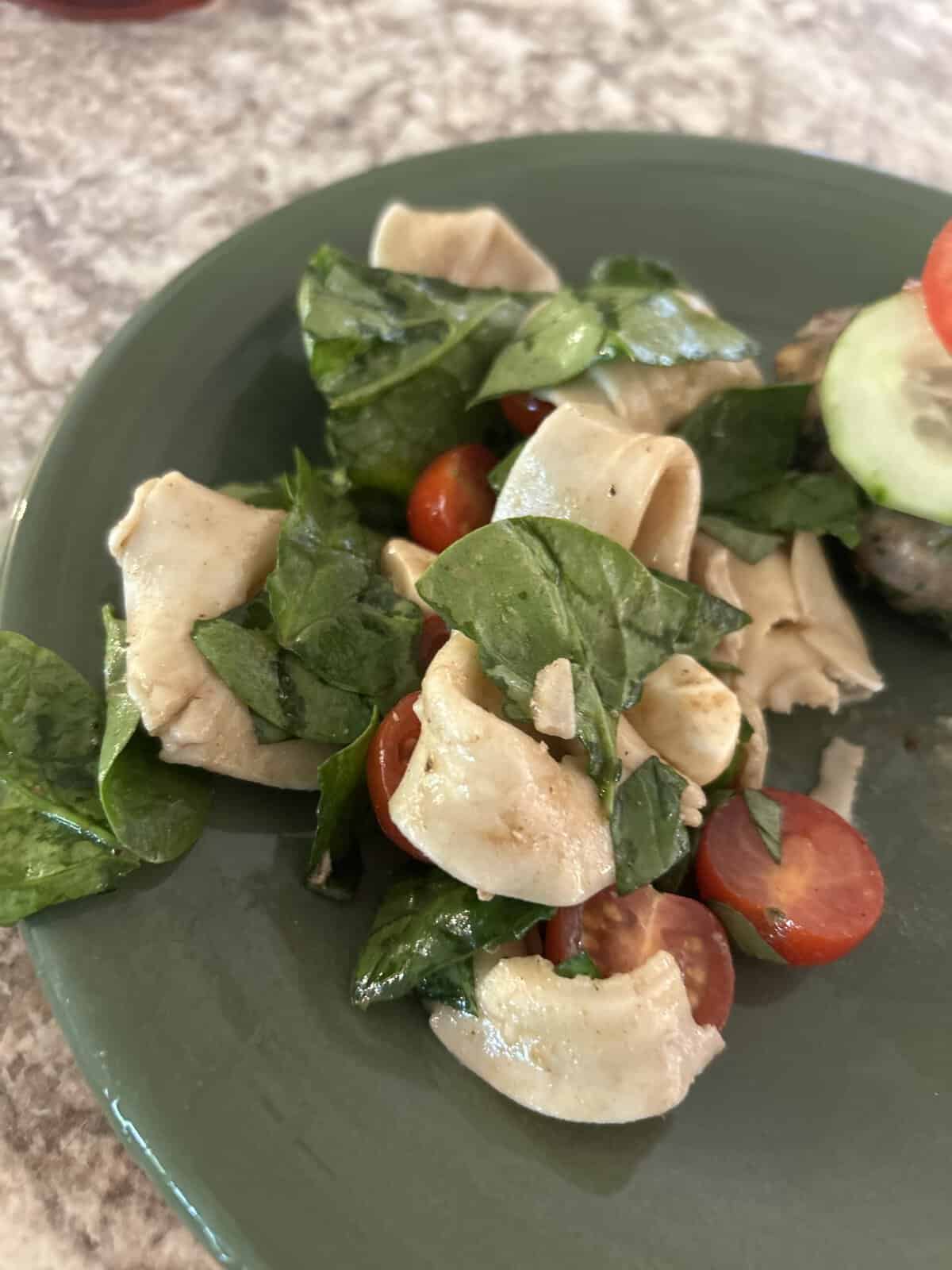 A salad with spinach, sliced grape tomatoes, and wide pasta ribbons on a green plate.