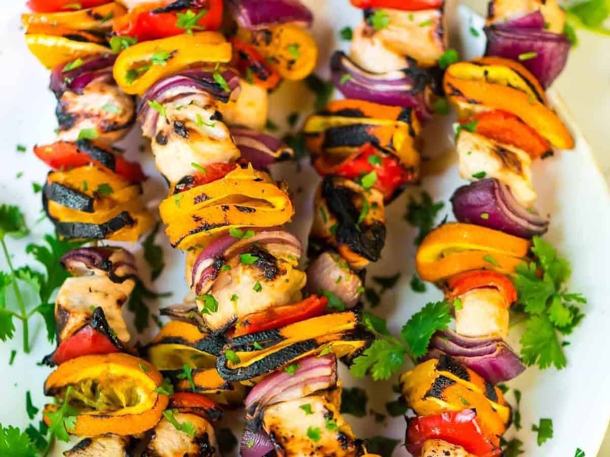 Five grilled orange kabobs on a white plate