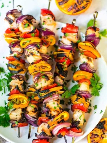 Five grilled orange kabobs on a white plate