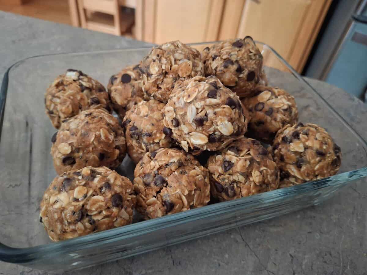 A glass dish filled with round oat and chocolate chip energy bites on a kitchen counter.