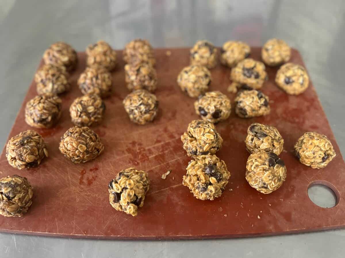 Twenty-one oatmeal chocolate chip energy bites arranged on a red cutting board on a metal surface.