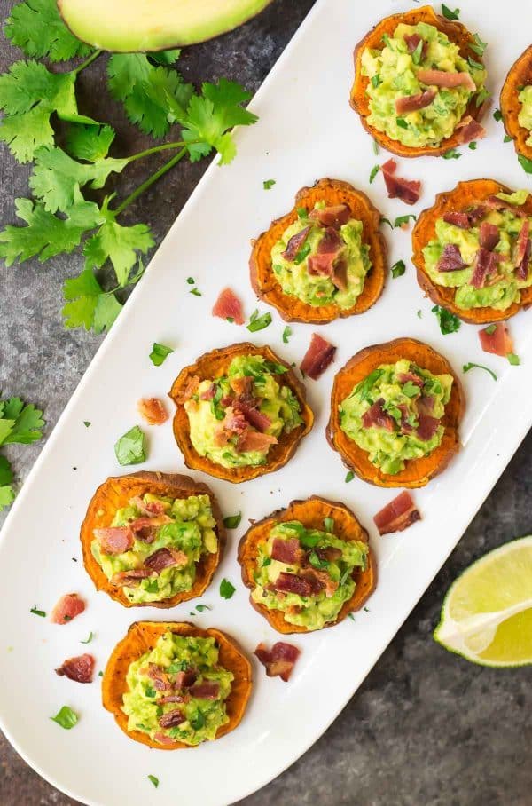 white platter of baked potato rounds topped with guacamole and bacon