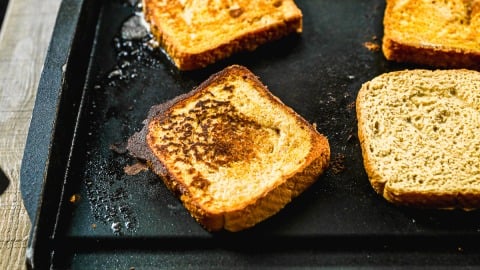 Slices of golden-brown pumpkin French toast cooking on a black griddle.