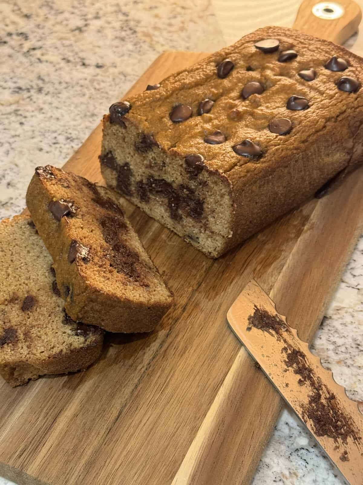 Chocolate chip loaf cake on a wooden cutting board, with two slices cut and a knife beside it.