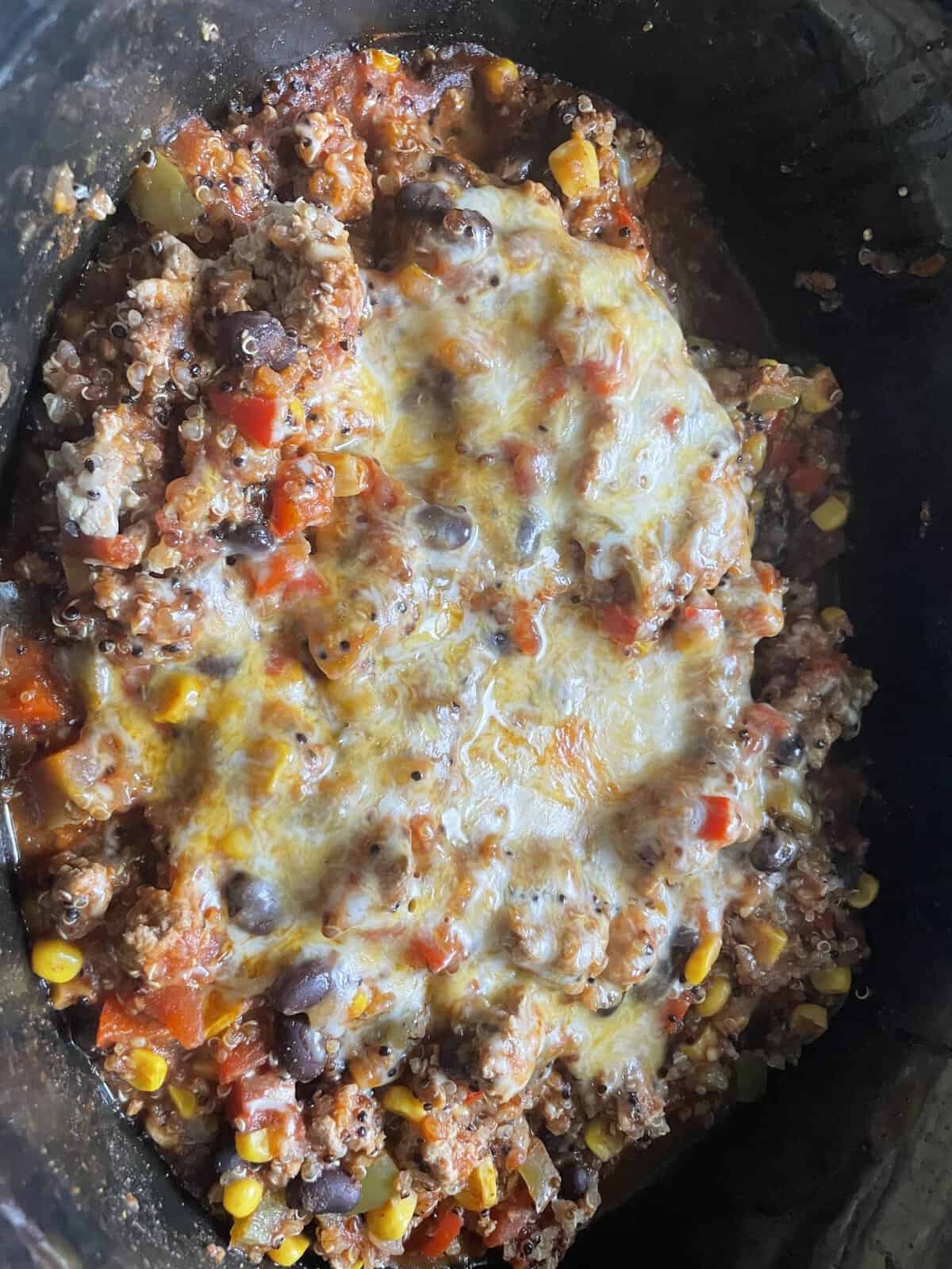 Casserole with melted cheese on top, black beans, corn, tomatoes, and ground meat in a black dish.