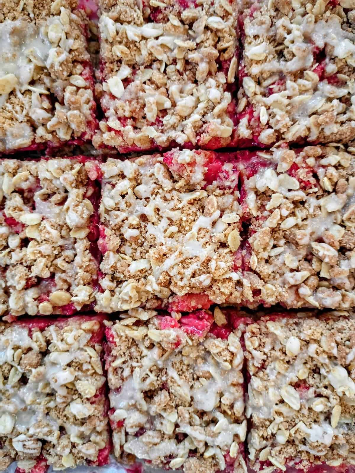 Close-up of nine oat crumble bars with a red fruit filling and light glaze, arranged in a grid pattern.