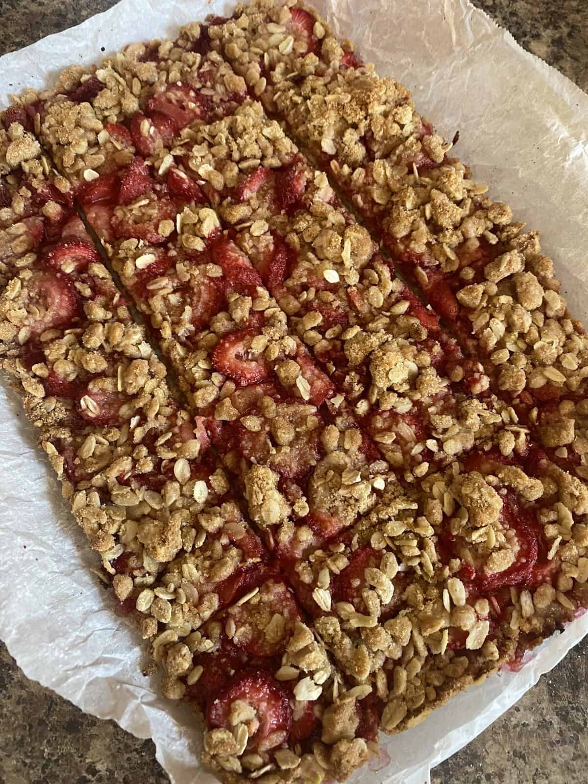 Strawberry oat crumble bars cut into rectangles on parchment paper, resting on a brown countertop.