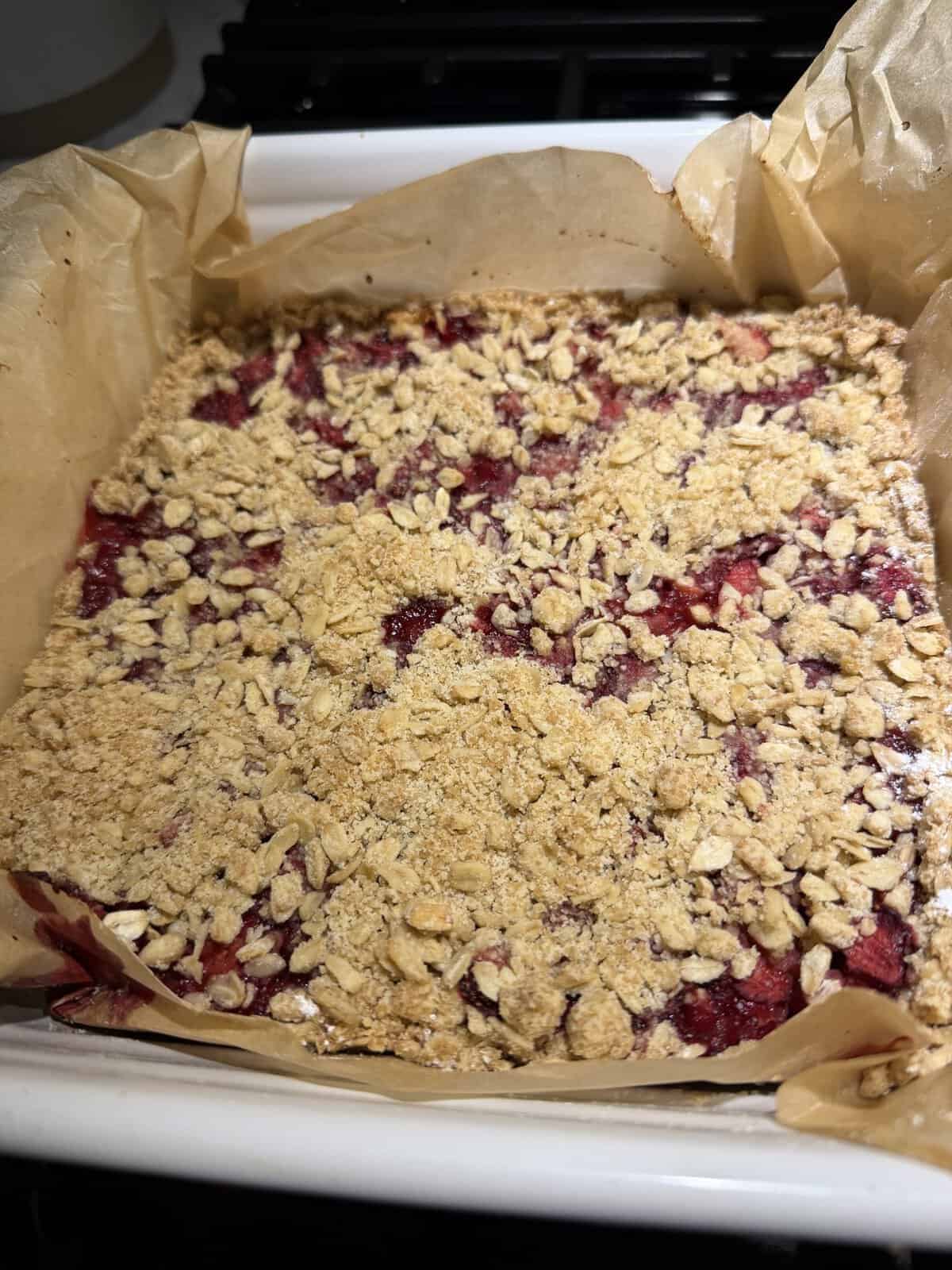 A close-up of a baked berry crumble in a parchment-lined dish, topped with oats and crumbly topping.