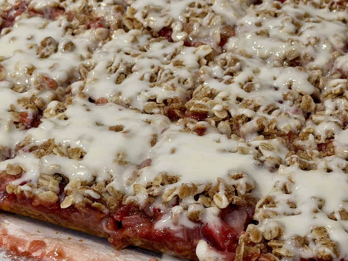 Close-up of strawberry oat bars topped with a white icing drizzle, cut into squares.