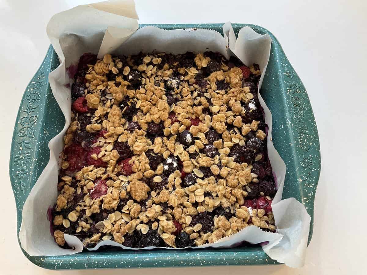 A square baking dish with a berry oat crumble lined with parchment paper, ready to be served.