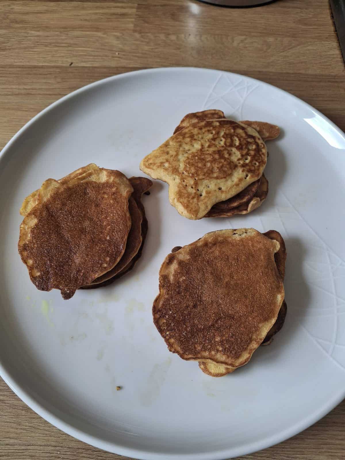 Three small stacks of pancakes on a white plate, placed on a wooden surface.
