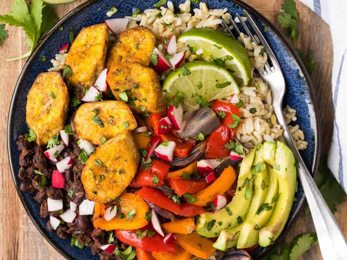 Nourishing Cuban Black Beans and Rice Bowls with baked plantains (tostones), roasted vegetables, and avocado. Packed with authentic Cuban flavors and ingredients. A healthy, filling, all-in-one recipe that’s vegan and gluten free!