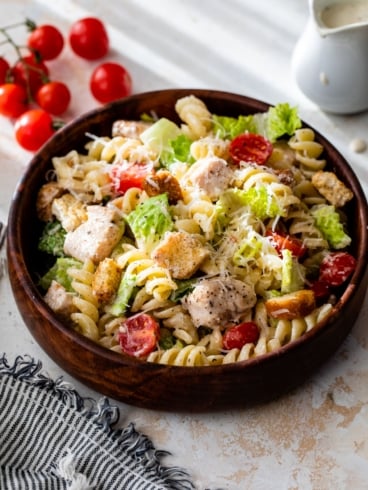 chicken Caesar salad in bowl with cherry tomatoes and dressing in background