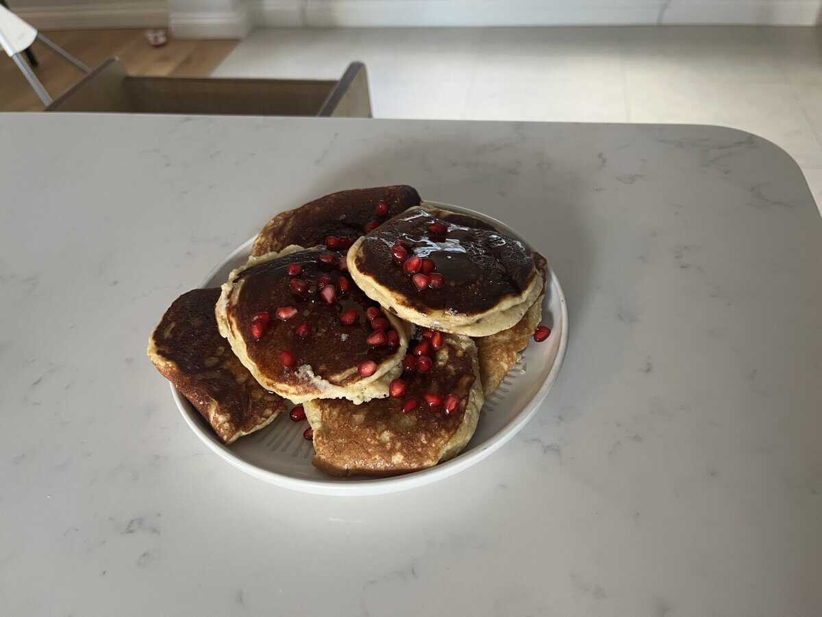 A plate of pancakes topped with pomegranate seeds sits on a white marble countertop.