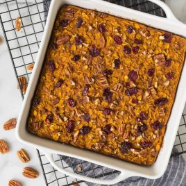 A square dish of baked oatmeal topped with pecans and dried cranberries on a cooling rack.