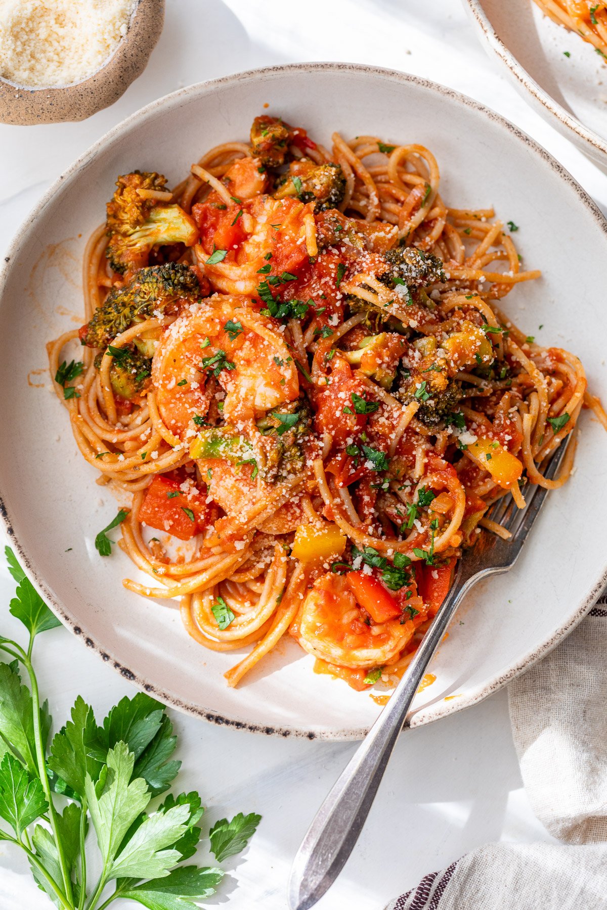 A plate of spicy shrimp pasta with tomato sauce, shrimp, broccoli, bell peppers, and parsley, with a fork on the plate.