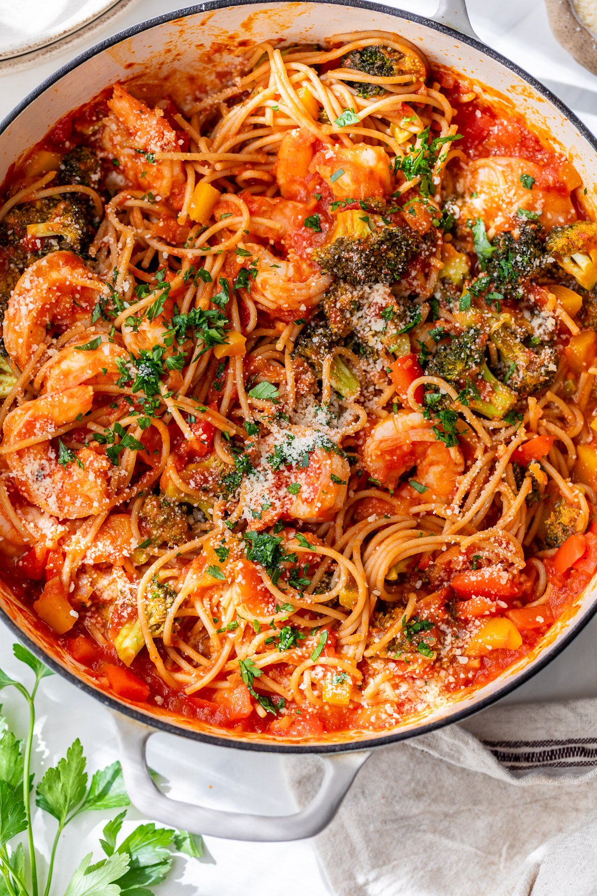 Spicy shrimp pasta with broccoli and tomato sauce, garnished with parsley and grated cheese in a white pot.