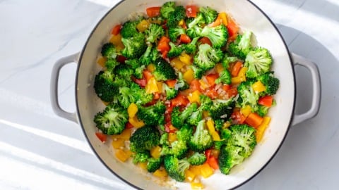 A pot filled with sautéed broccoli, red bell pepper, and yellow bell pepper on a light surface.