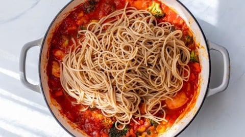 Spaghetti on top of vegetable tomato sauce in a white pot, ready to be mixed together for spicy shrimp pasta.