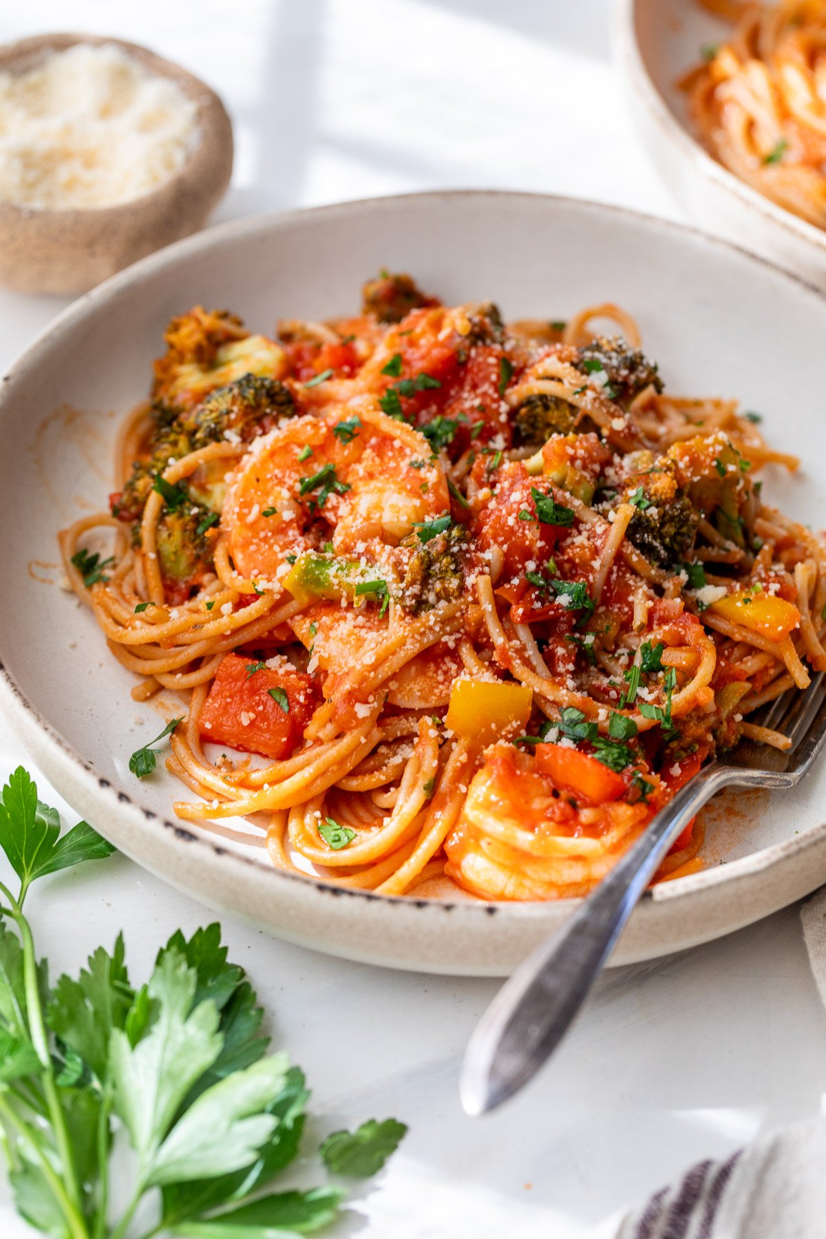 A plate of spicy shrimp pasta with tomato sauce, vegetables, and herbs, topped with grated cheese and served with a fork.