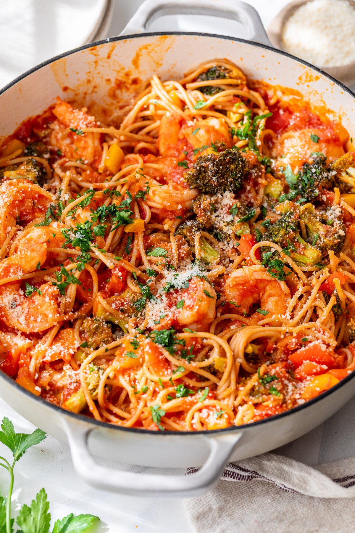 Spicy shrimp pasta with broccoli and tomato sauce, garnished with parsley and grated cheese in a white pot.