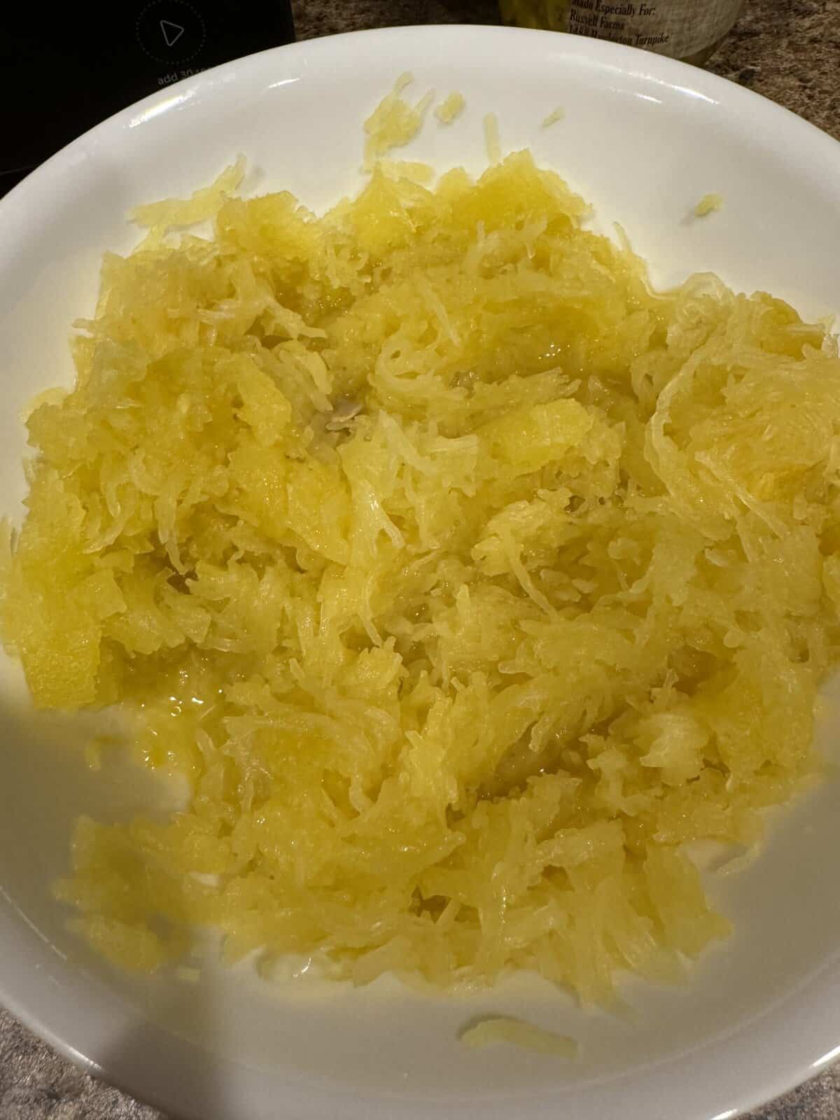 Cooked spaghetti squash shredded into strands in a white bowl, ready to be served or used in a recipe.