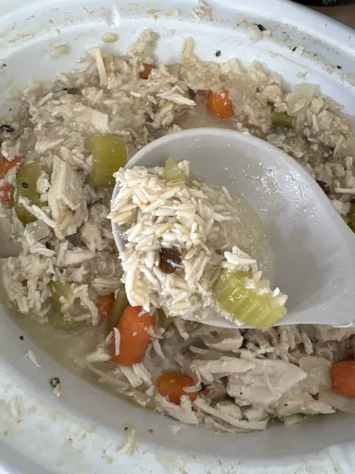 A ladle scoops chicken, rice, carrots, and celery from a pot of homemade chicken and rice soup.