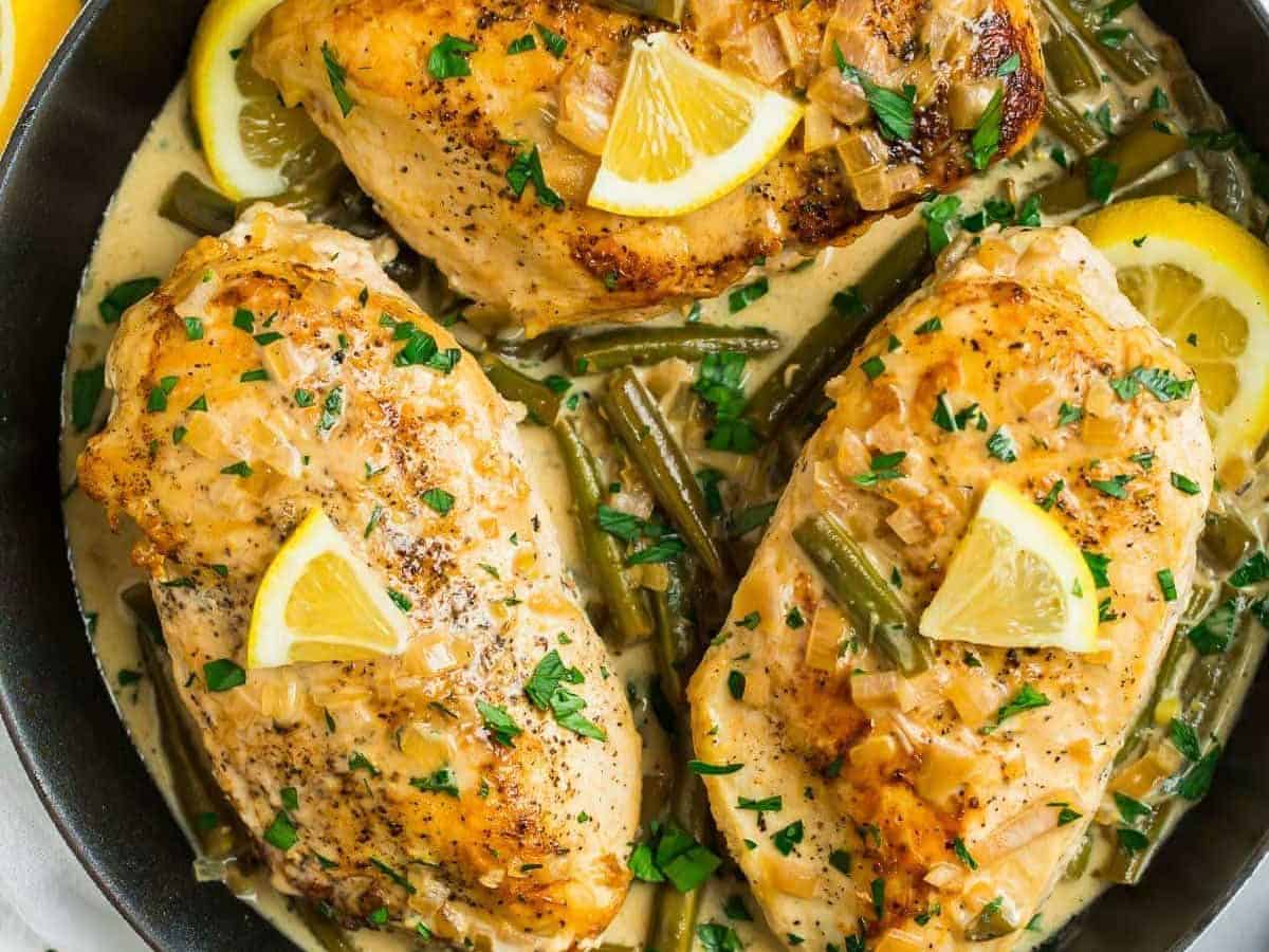 A skillet with three chicken breasts in a lemon butter sauce