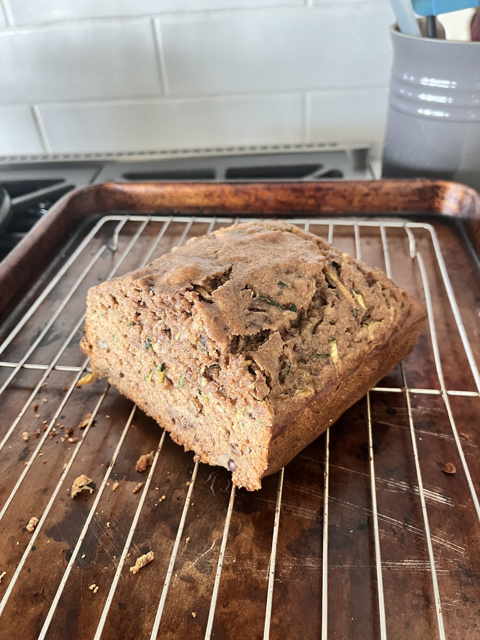 A loaf of zucchini bread cooling on a wire rack over a baking sheet in a kitchen.