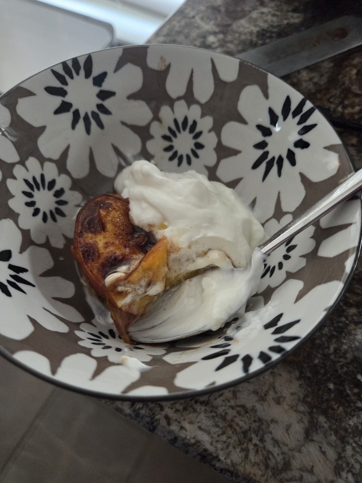 A patterned bowl with yogurt and a piece of baked pastry, with a spoon resting inside.