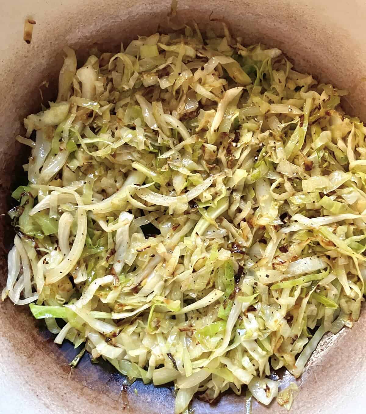 Sautéed shredded cabbage in a pan, lightly browned and seasoned with black pepper.