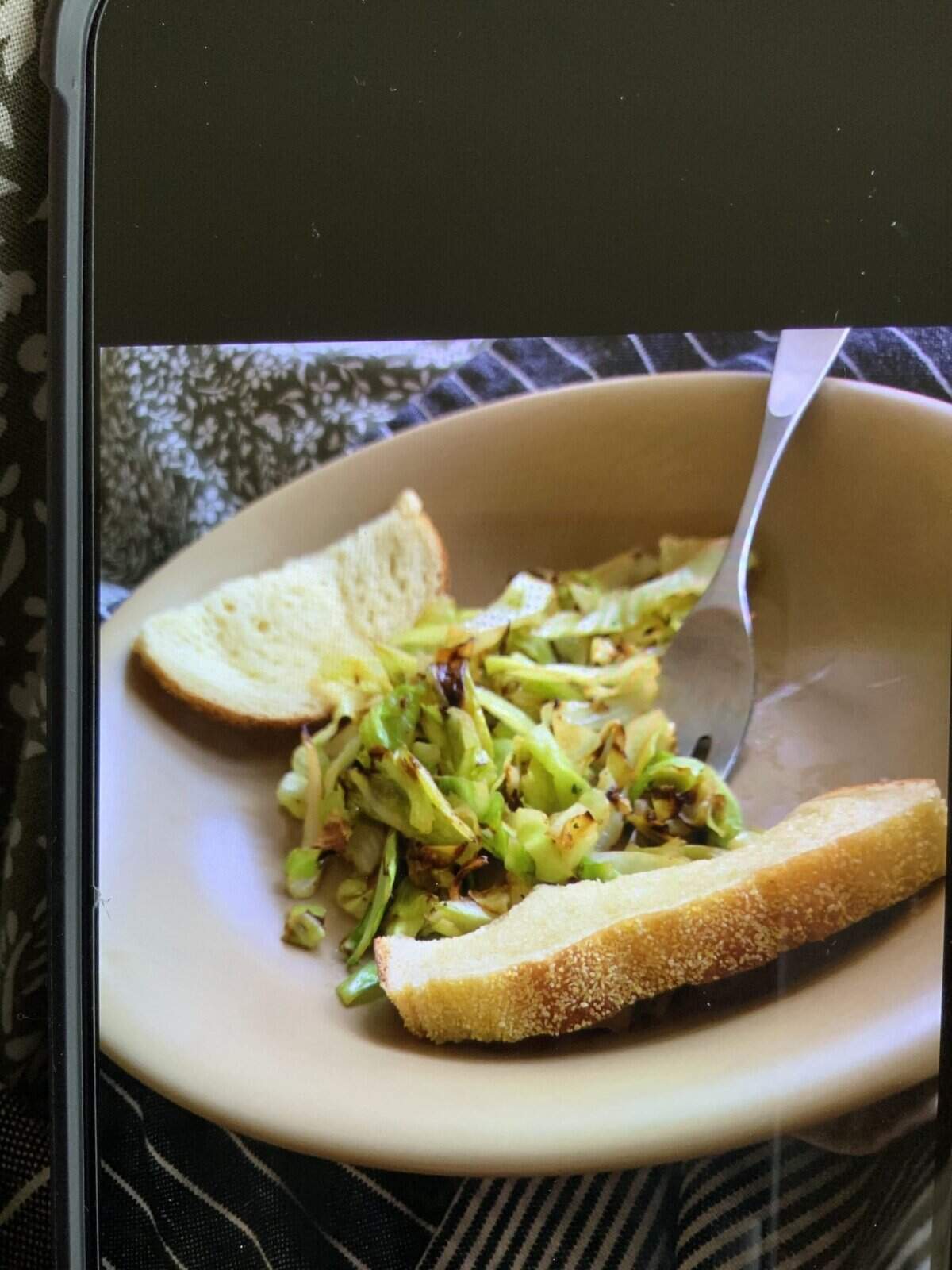 A bowl with sautéed cabbage, a fork, and two slices of bread on the side.
