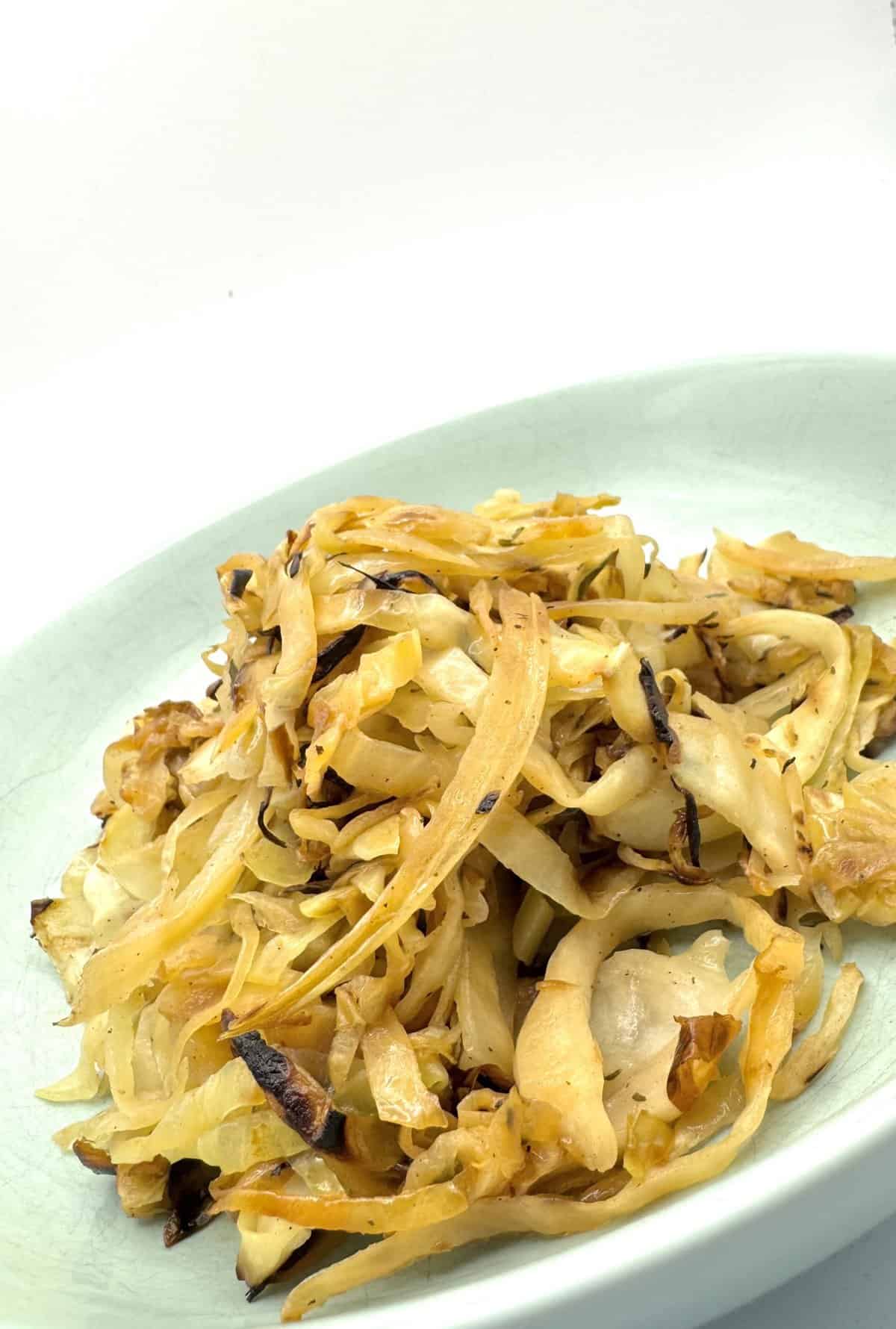 A plate of cooked, shredded cabbage with browned edges on a pale green dish, set against a white background.