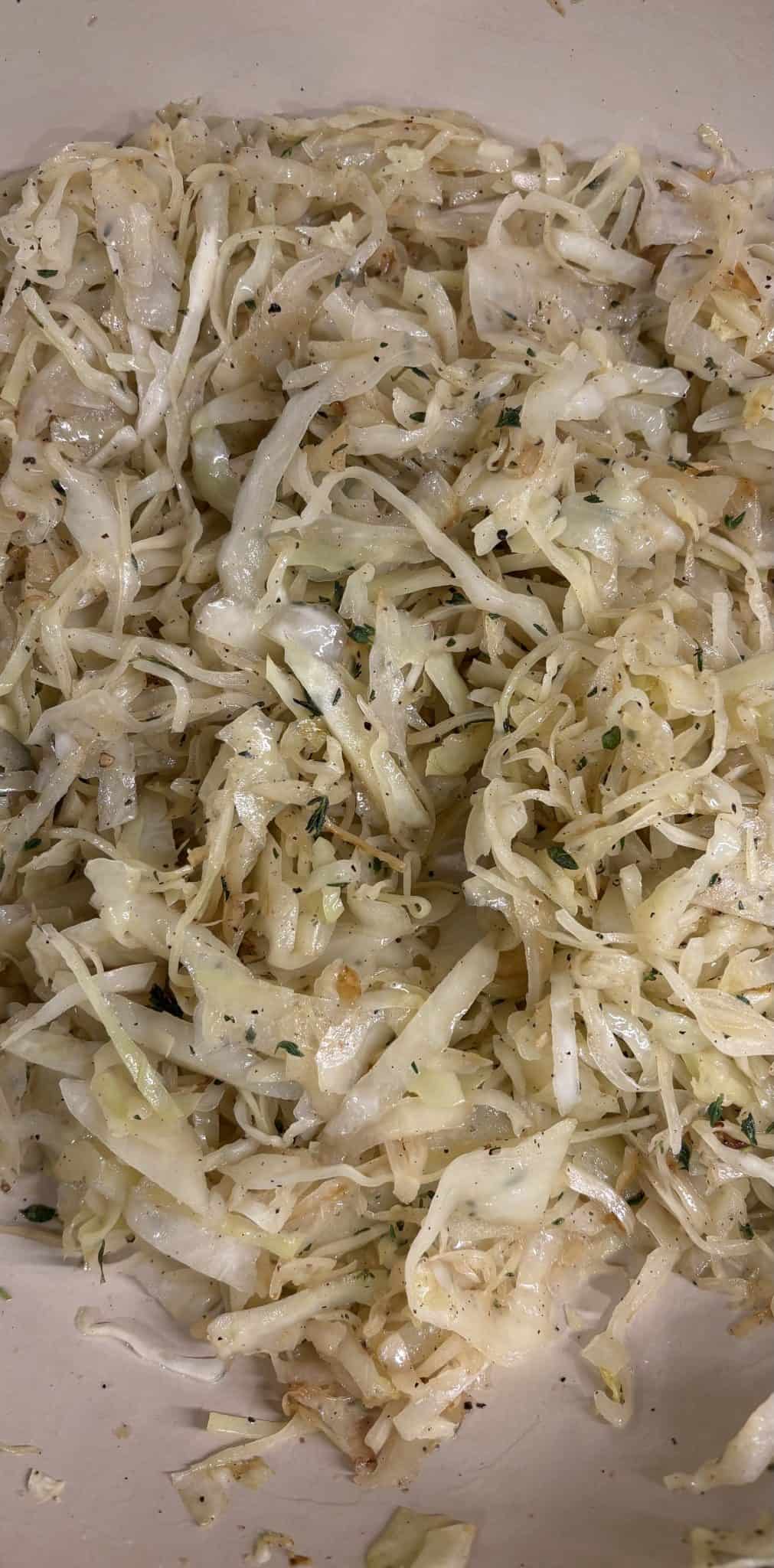 Close-up of cooked shredded cabbage with herbs and black pepper in a white dish.