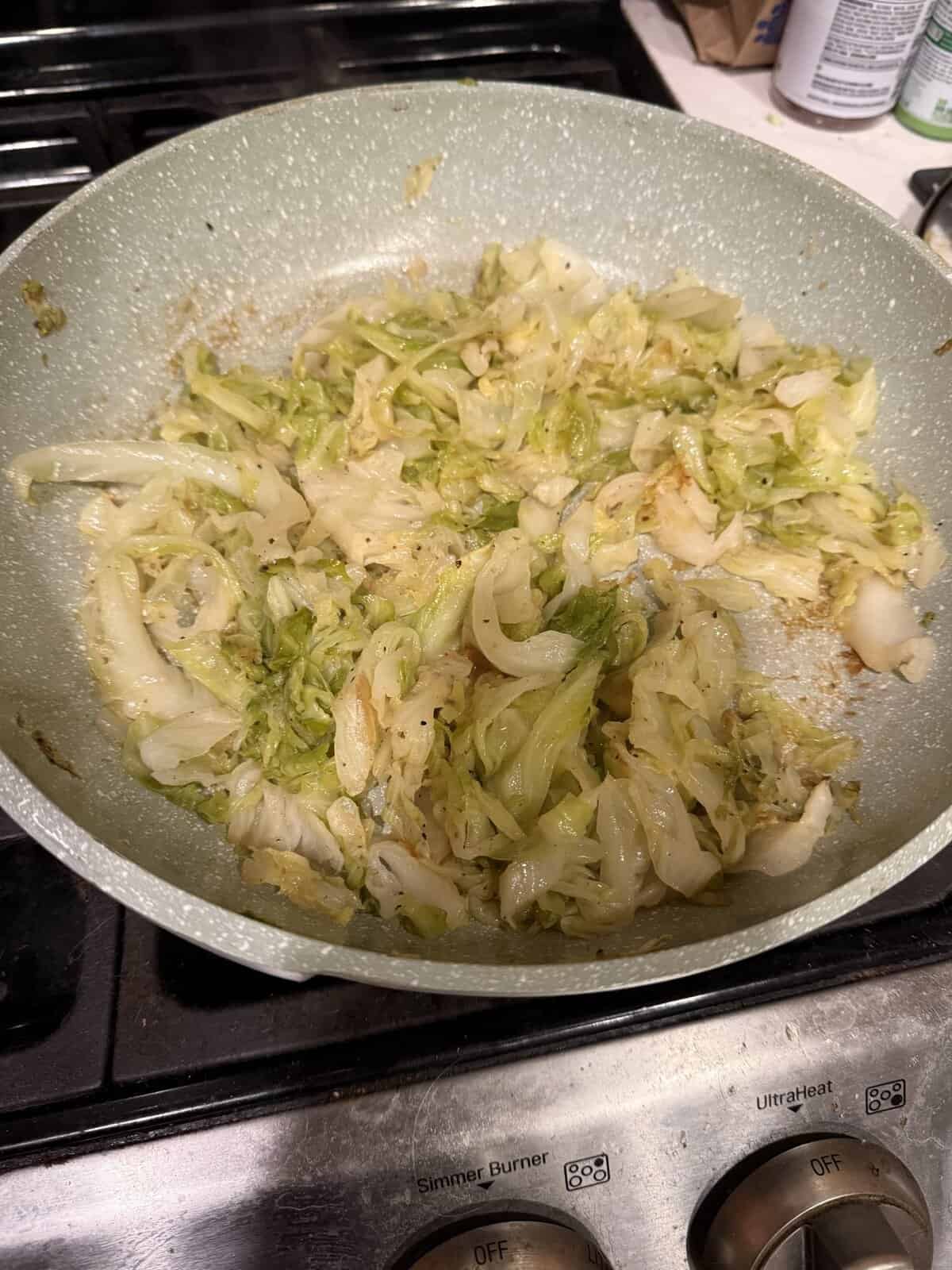 Sautéed cabbage cooking in a light-colored frying pan on a stovetop.