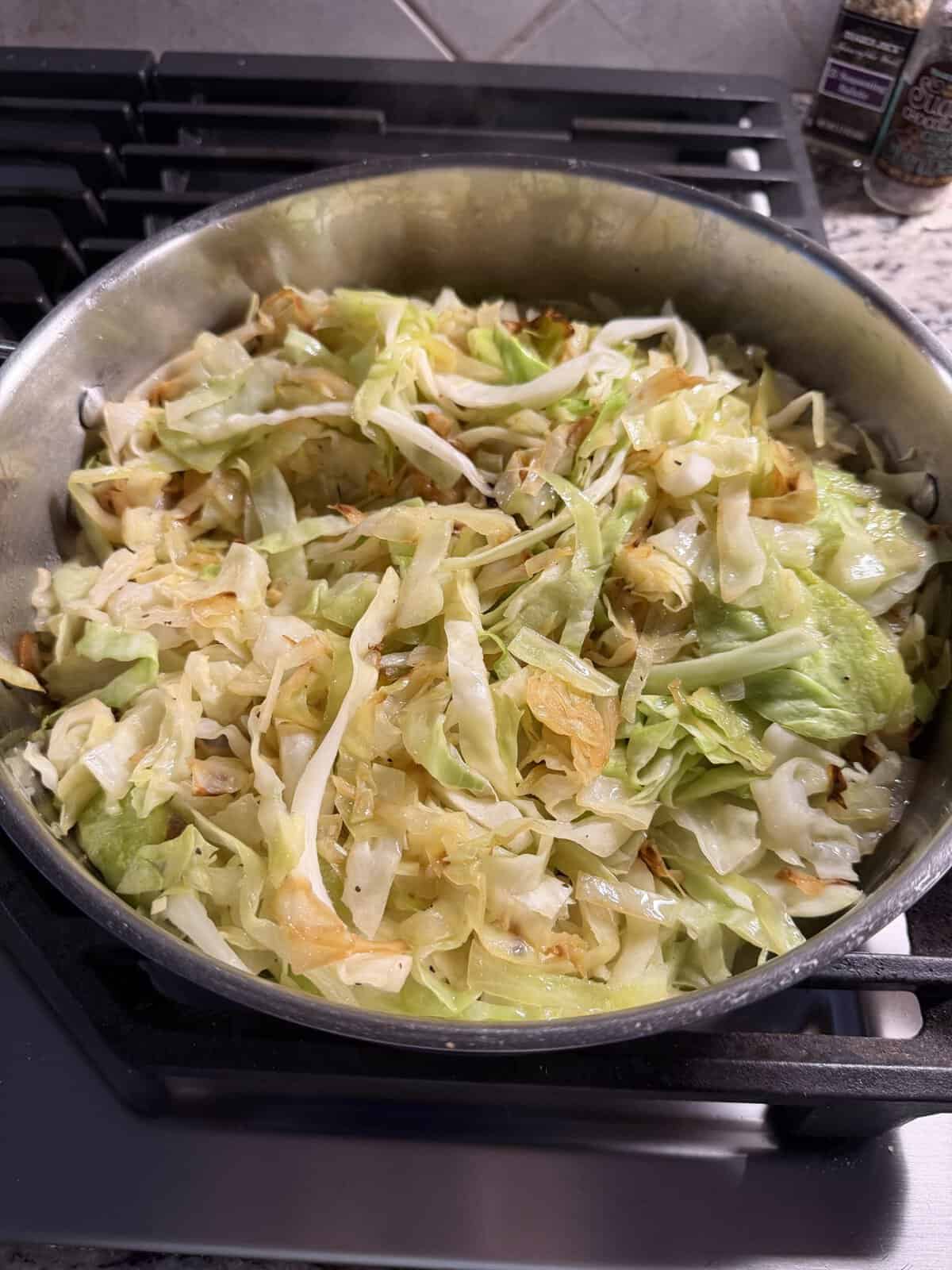 Sautéed cabbage cooking in a stainless steel skillet on a stovetop.