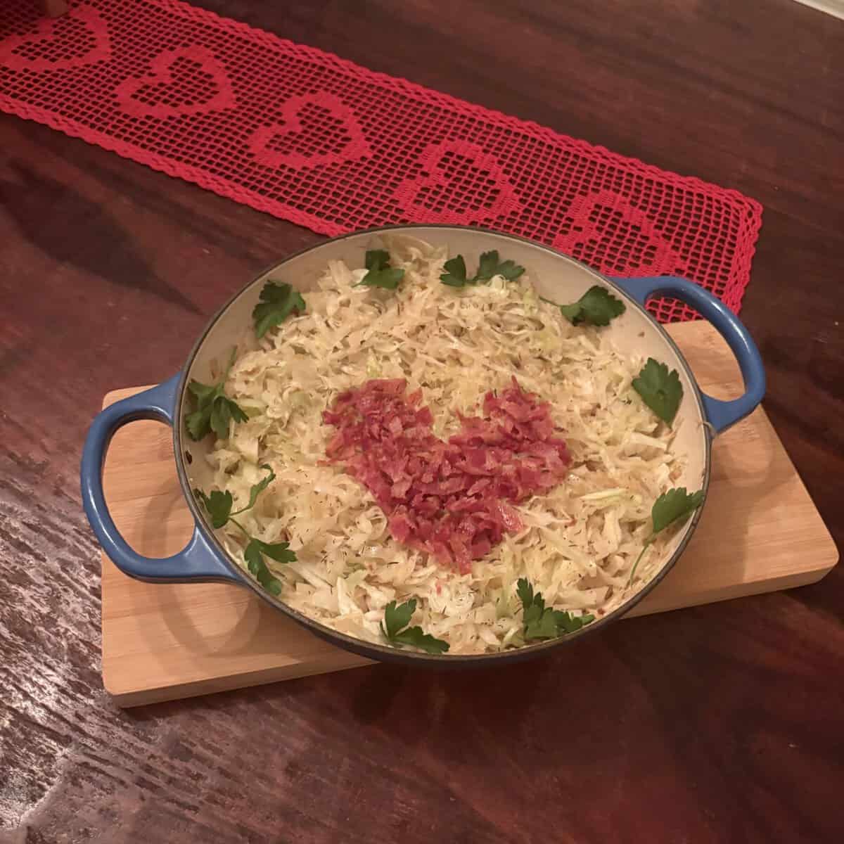 A casserole with a heart shape made of ham, garnished with parsley, sits on a wooden board on a table.